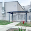 Full height turnstiles and full height gate installed under a canopy outside of a factory in a fence line