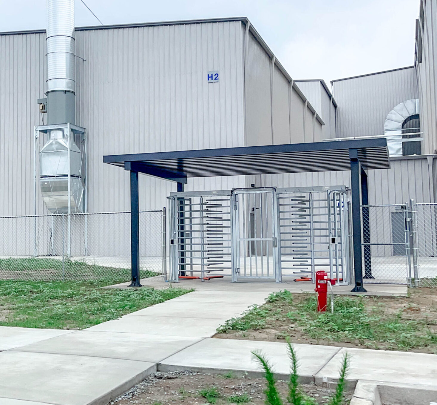 Full height turnstiles and full height gate installed under a canopy outside of a factory in a fence line