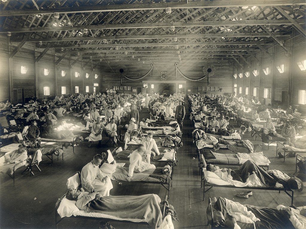 Spanish flu patients in hospital beds lining an auditorium in black and white