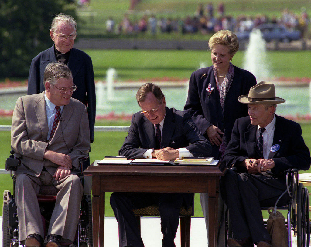 George HW Bush signing the Americans with disabilities act in 1990 with one disabled individual on either side of him